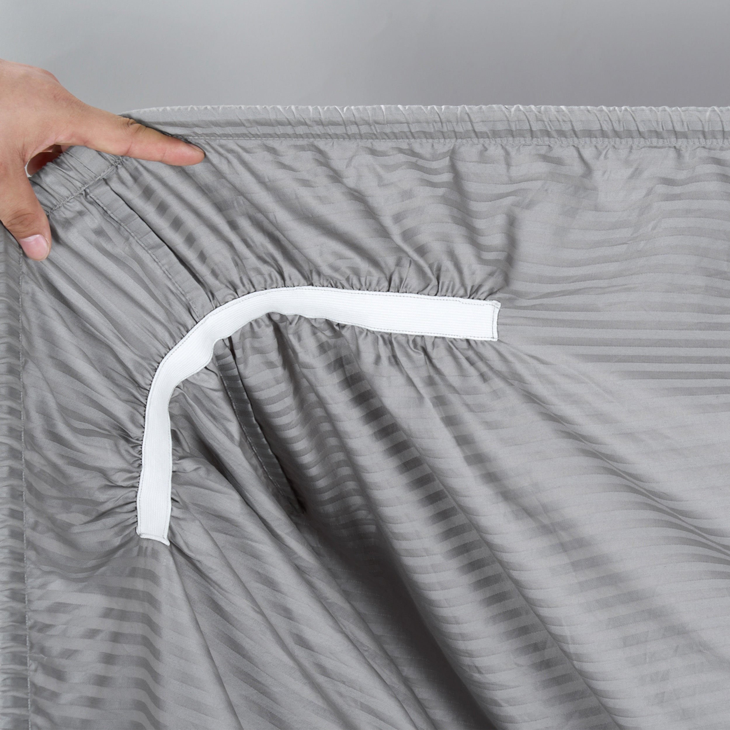 Gray pants with a white waistband being adjusted by a hand on a gray background