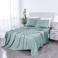Teal bedspread and pillow set on a bed in a bedroom with a lamp and plant.