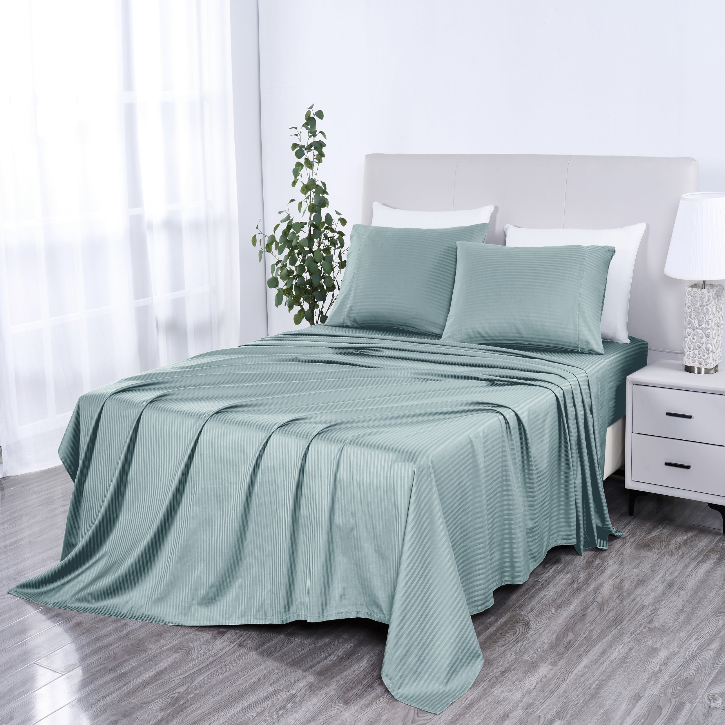 Teal bedspread and pillow set on a bed in a bedroom with a lamp and plant.