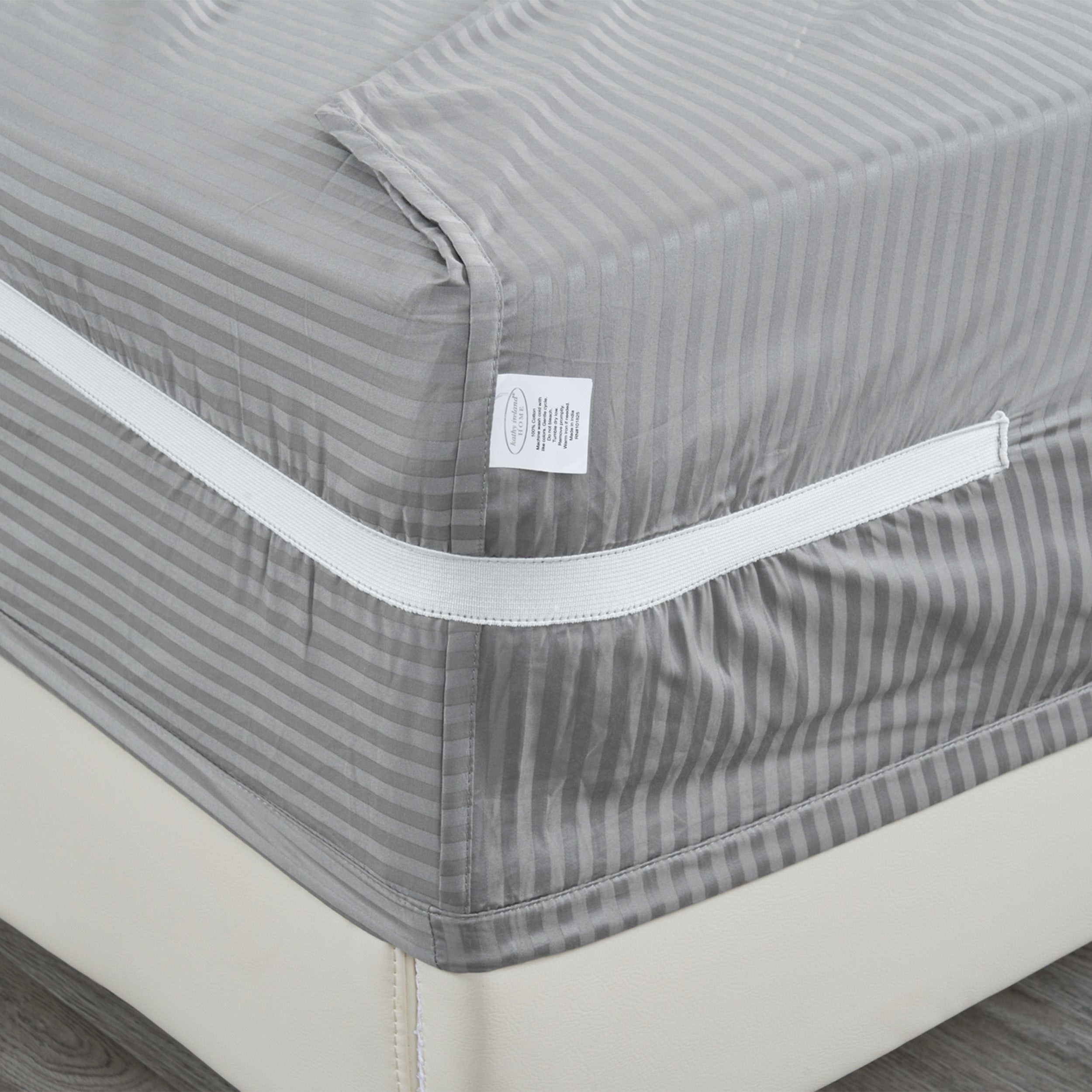 Gray striped mattress cover with a visible brand label on a bed.