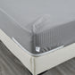Gray striped mattress cover on a bed with a wooden floor.