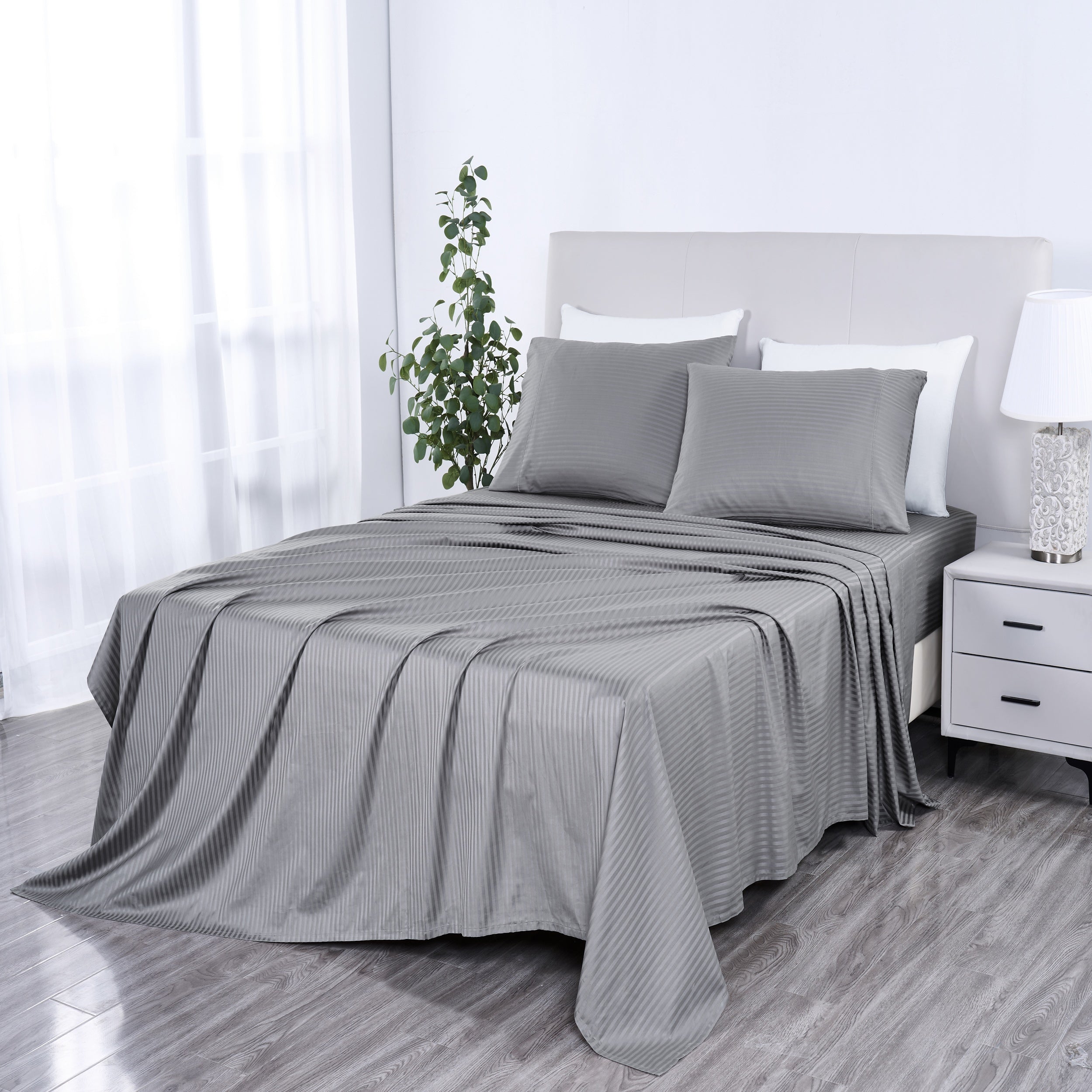 Gray striped bedspread on a bed in a bedroom setting with white walls and a nightstand.