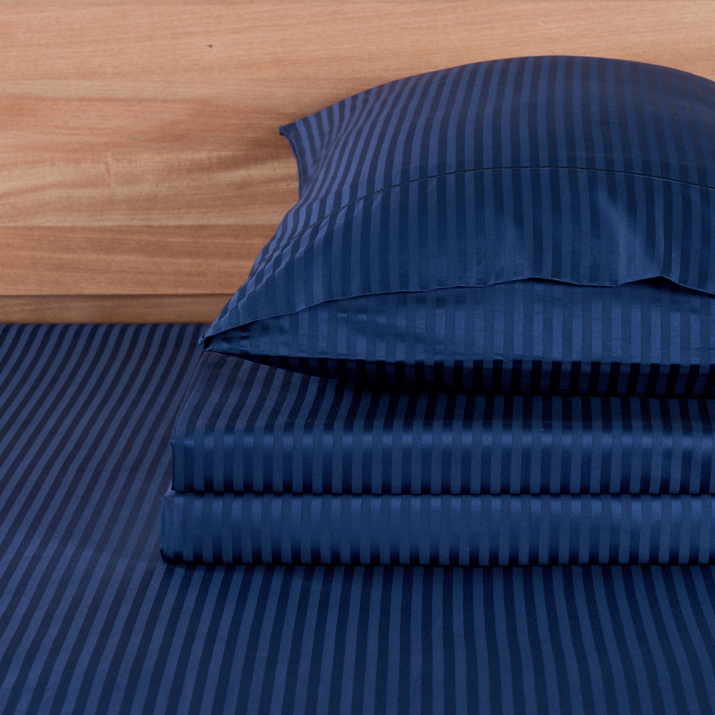 Blue striped bed sheets and pillowcase set on a wooden bed frame.