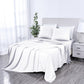 White bedspread on a bed in a bright bedroom with a plant and nightstand.