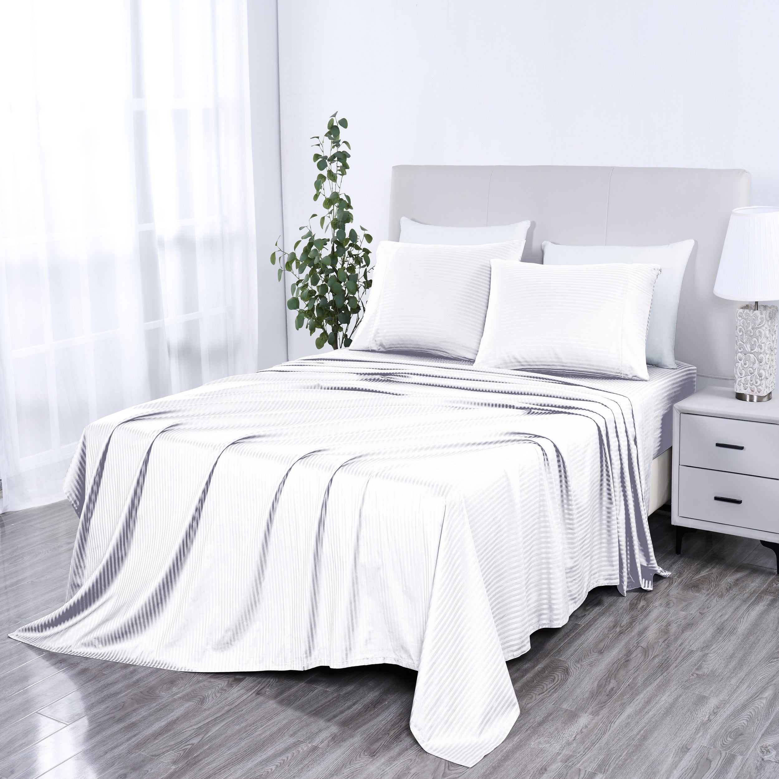White bedspread on a bed in a bright bedroom with a plant and nightstand.