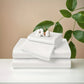 Stack of white folded sheets on a light surface with green leaves in the background