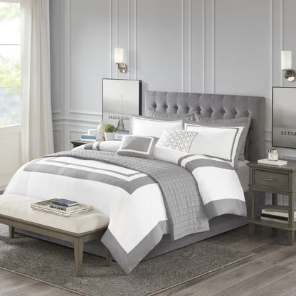 Gray and white bedding set on a bed in a bedroom with matching headboard and nightstands.