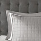 Quilted gray pillow on a bed with a tufted headboard