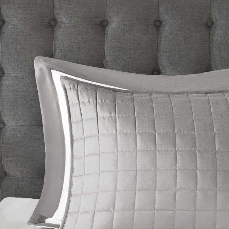 Quilted gray pillow on a bed with a tufted headboard