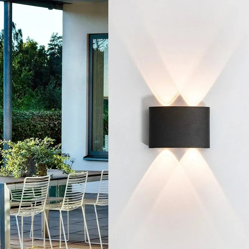 Modern outdoor wall light fixture on a white wall with a view of a patio and garden.