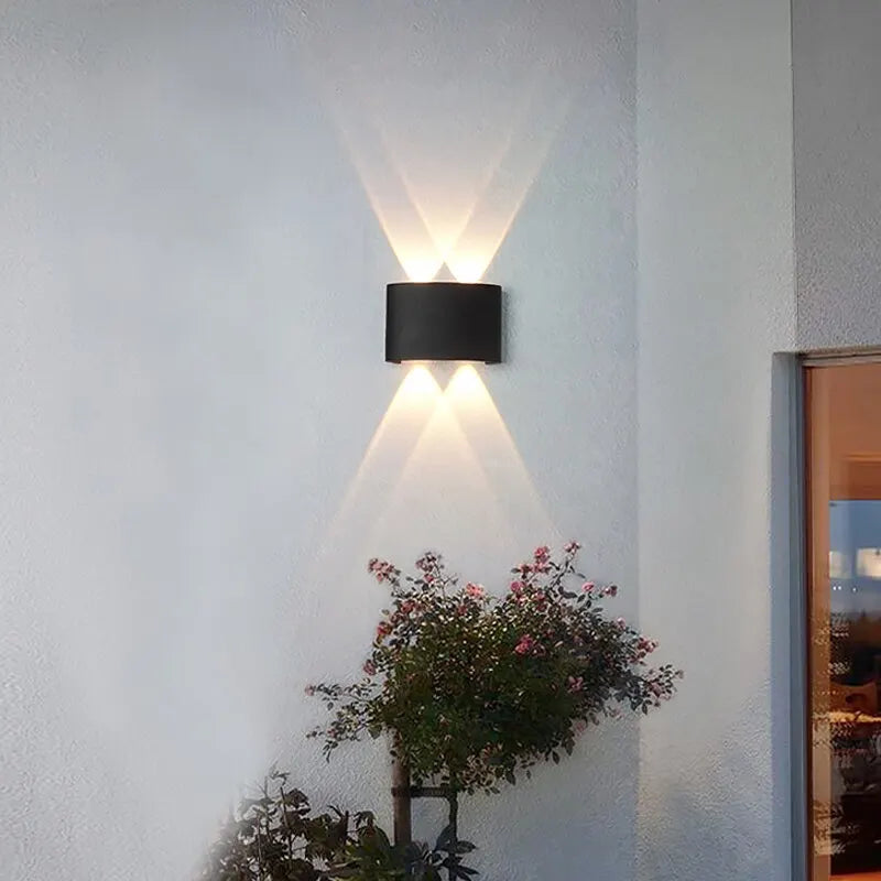 Modern wall-mounted light fixture on a white wall with plants below.