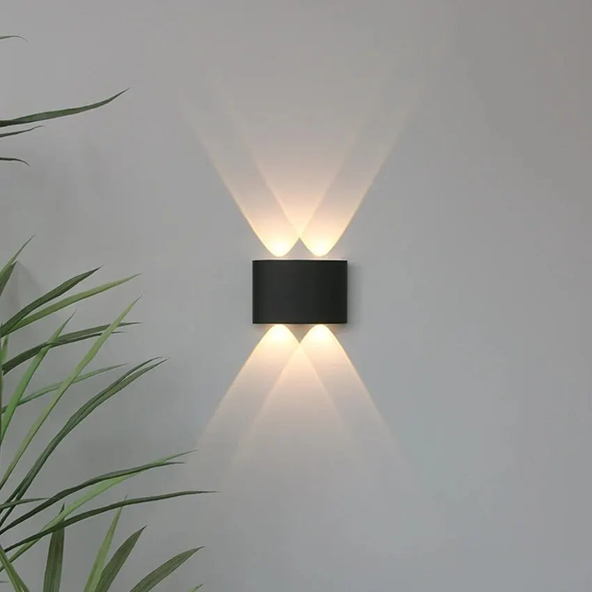 Modern wall-mounted light fixture on a plain wall with a plant in the corner.