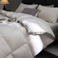 White quilted comforter on a bed with gray and white pillows in a dimly lit room.