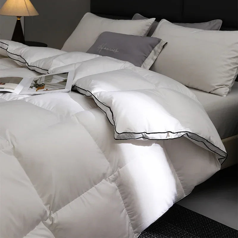 White quilted comforter on a bed with gray and white pillows in a dimly lit room.