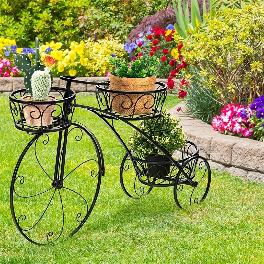 Black metal bicycle-shaped plant stand with three pots on a grassy area with flowers in the background