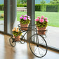Decorative metal plant stand with three potted plants in front of a large window with a garden view.