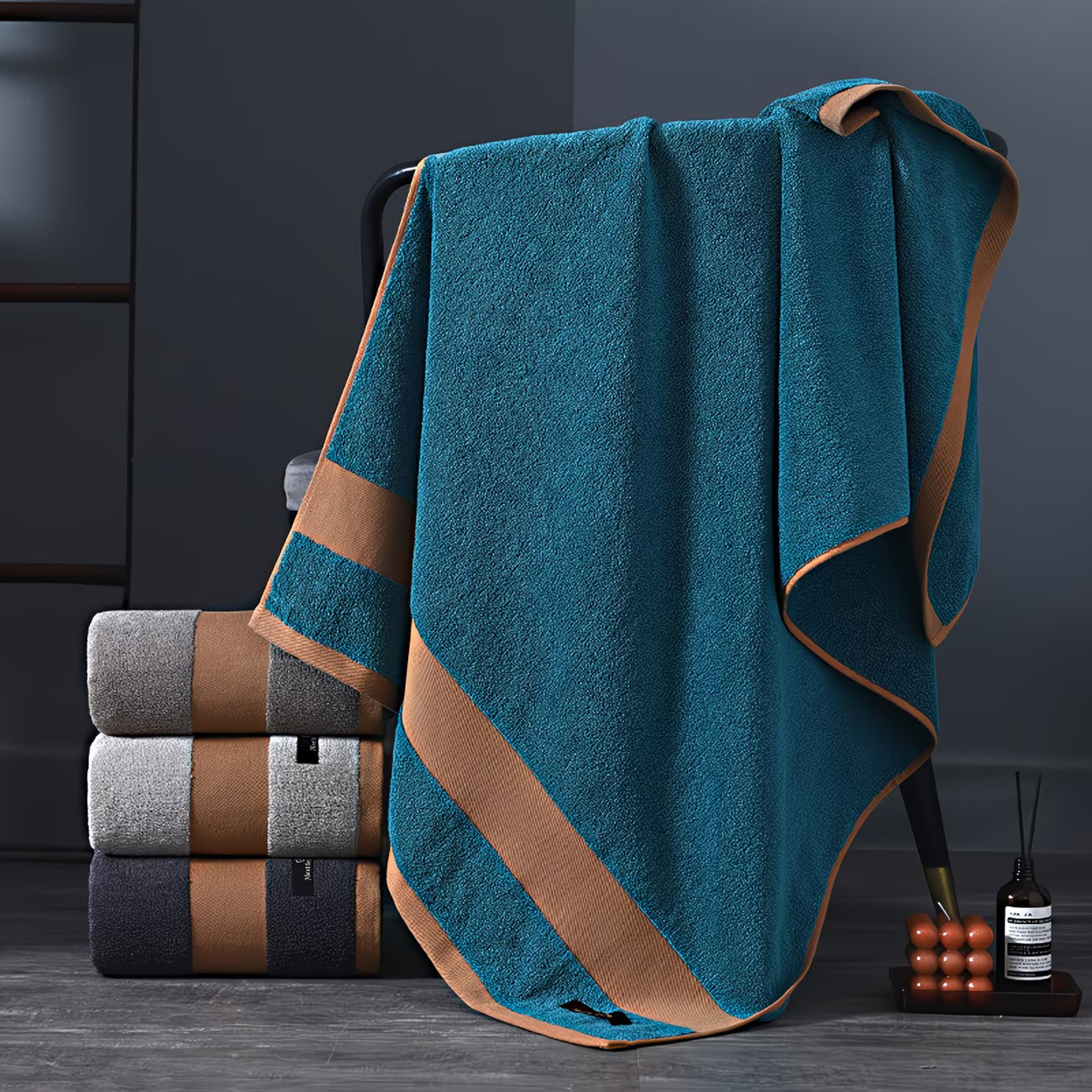 Teal towel with brown trim draped over a stack of folded towels on a dark surface.