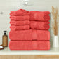Stack of red towels on a bathroom counter with a soap dispenser and decorative plant.