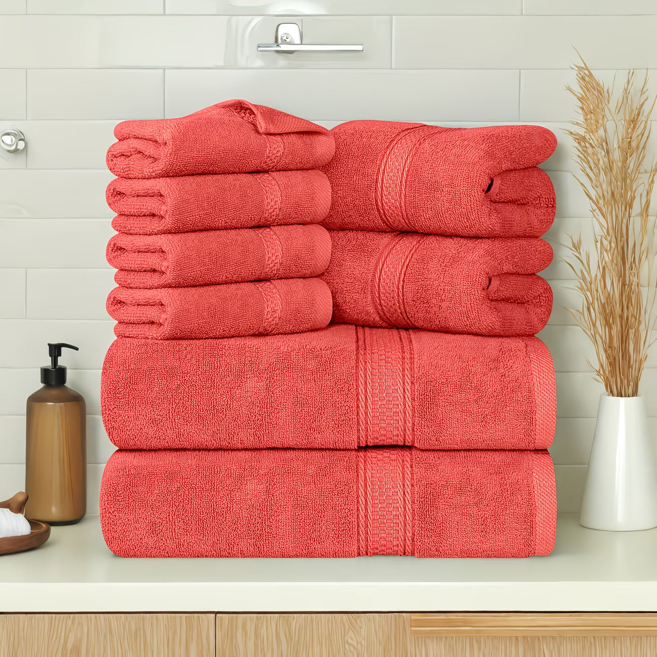 Stack of red towels on a bathroom counter with a soap dispenser and decorative plant.