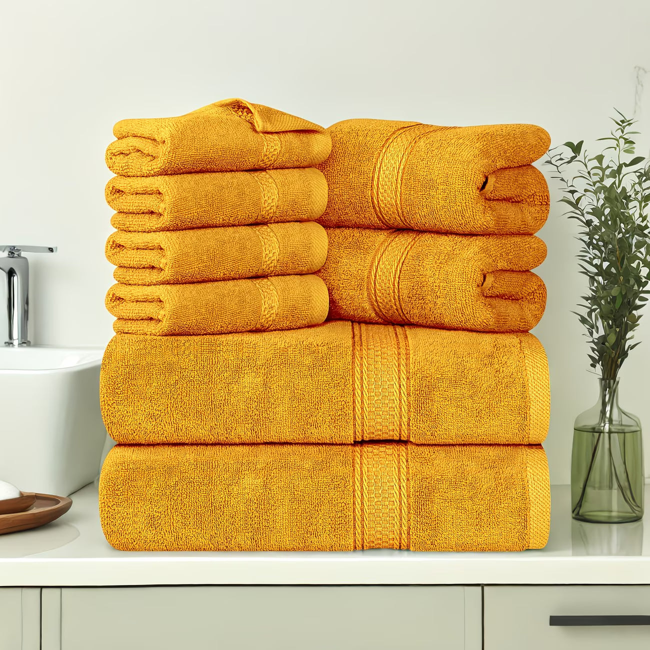 Stack of yellow towels on a bathroom counter with a vase and sink in the background.