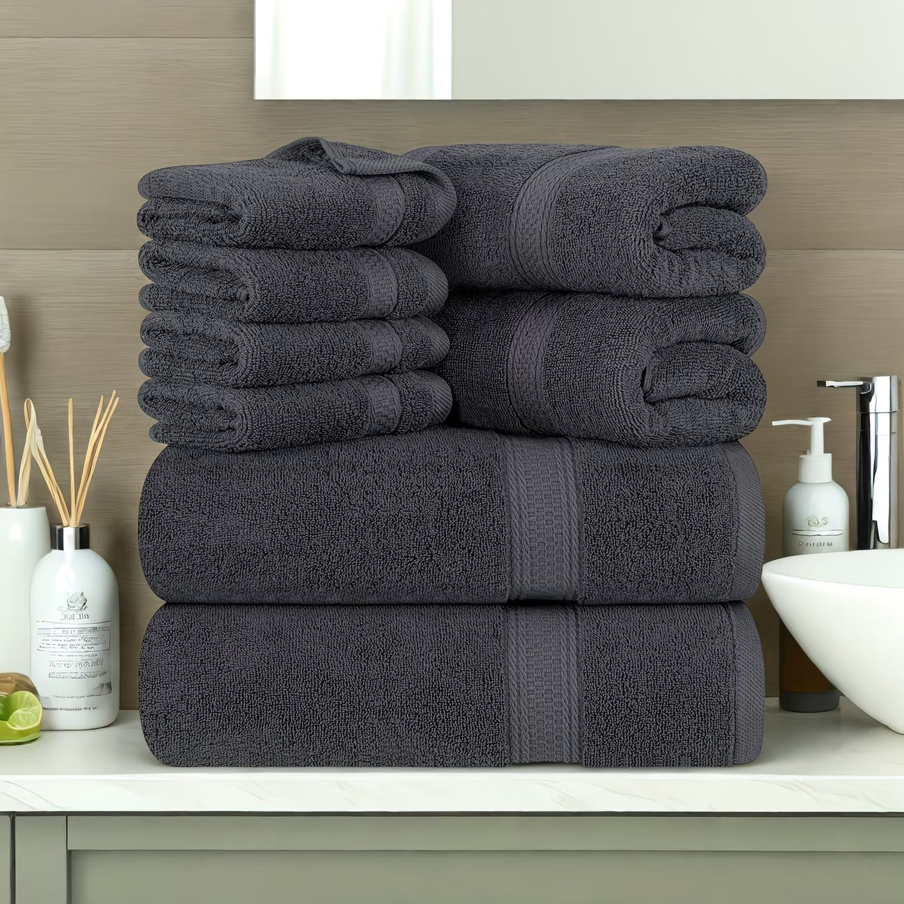 Stack of dark gray towels on a bathroom counter with various items in the background.