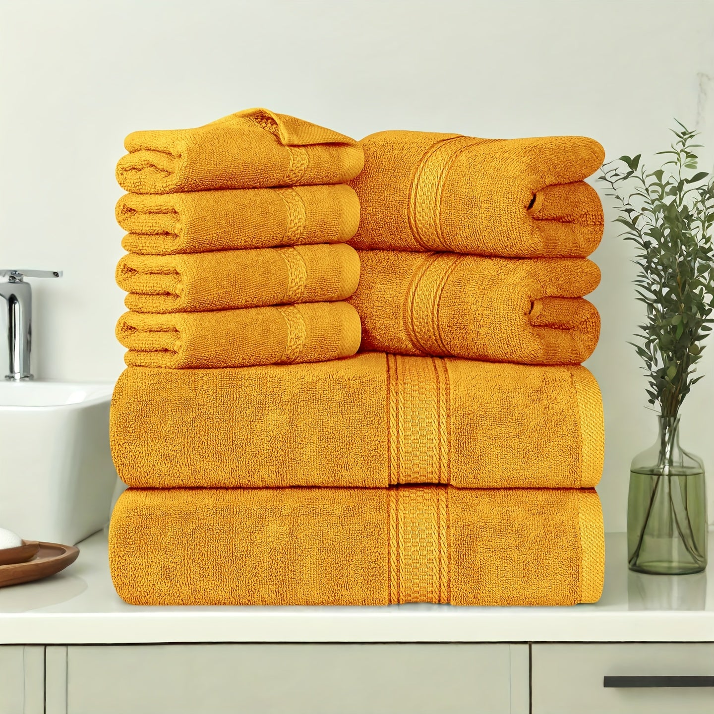 Stack of yellow towels on a bathroom counter with a sink and plant in the background.