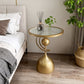 Gold side table with a glass top next to a bed in a bedroom setting