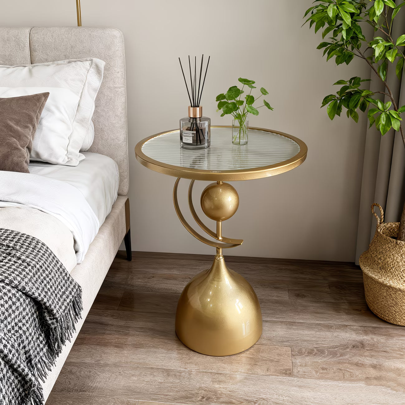 Gold side table with a glass top next to a bed in a bedroom setting