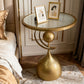 Gold side table with round glass top in a bedroom setting