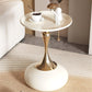 Modern side table with gold base and white top, featuring a cup of coffee and decorative items.