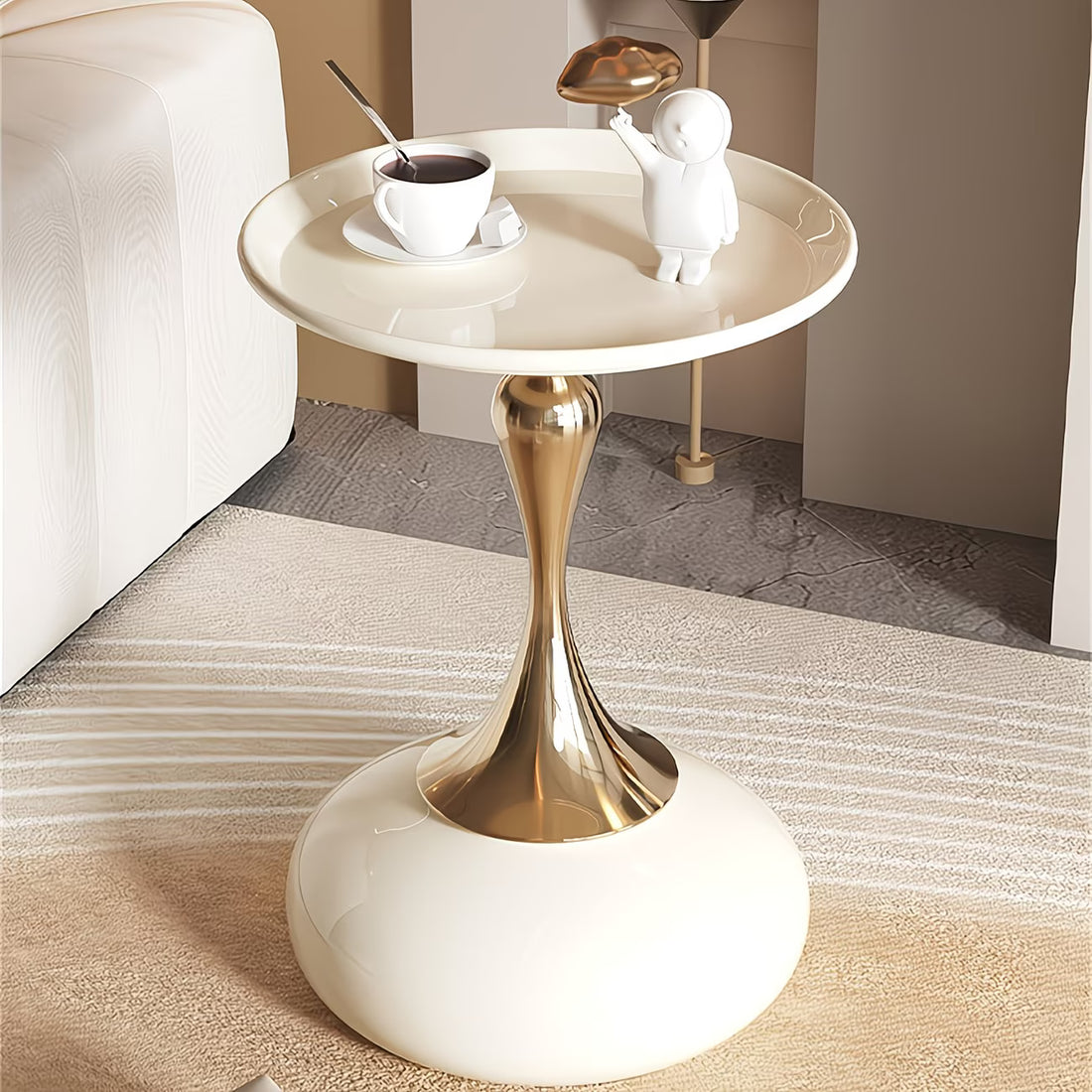 Modern side table with gold base and white top, featuring a cup of coffee and decorative items.