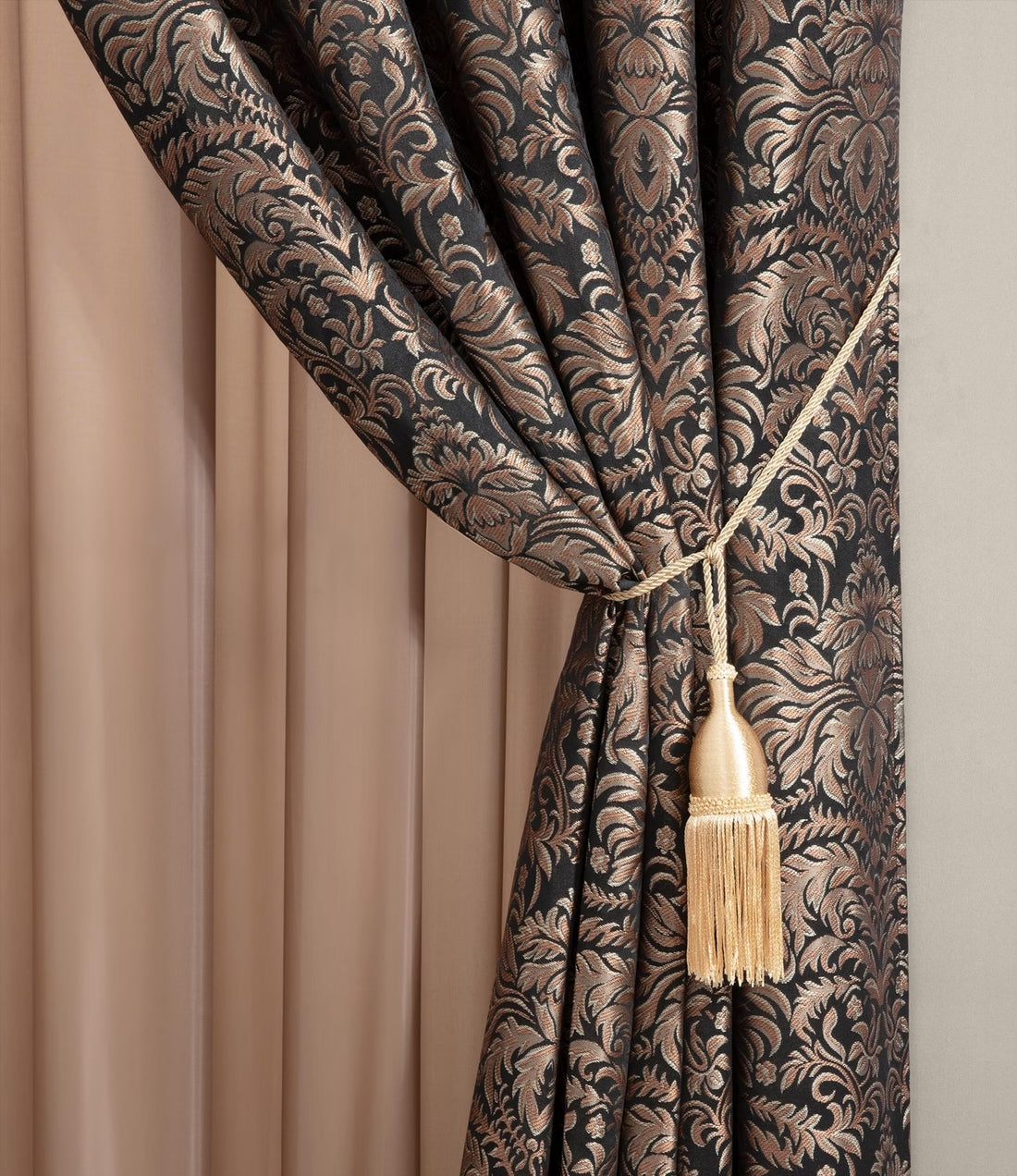 Decorative curtain with intricate pattern and tassel tieback against a neutral background