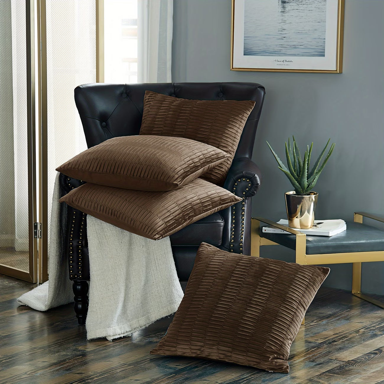 Brown textured pillows on a black leather armchair in a room with a plant and side table.