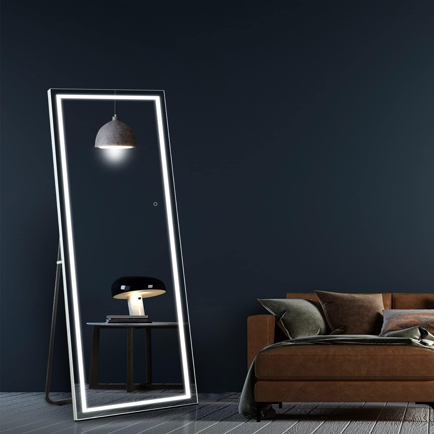 Large illuminated standing mirror in a room with a dark wall and brown sofa.