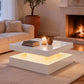 Modern living room with a white coffee table, books, and a candle in front of a fireplace.