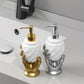 Two decorative soap dispensers shaped like hands, one gold and one silver, on a bathroom counter.