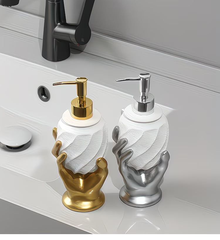 Two decorative soap dispensers shaped like hands, one gold and one silver, on a bathroom counter.