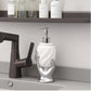 Silver hand-shaped soap dispenser on a kitchen counter with a faucet and shelves in the background.