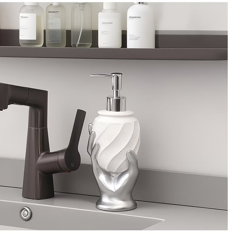 Silver hand-shaped soap dispenser on a kitchen counter with a faucet and shelves in the background.