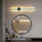 Modern wall light fixture above a round mirror in a bathroom setting.