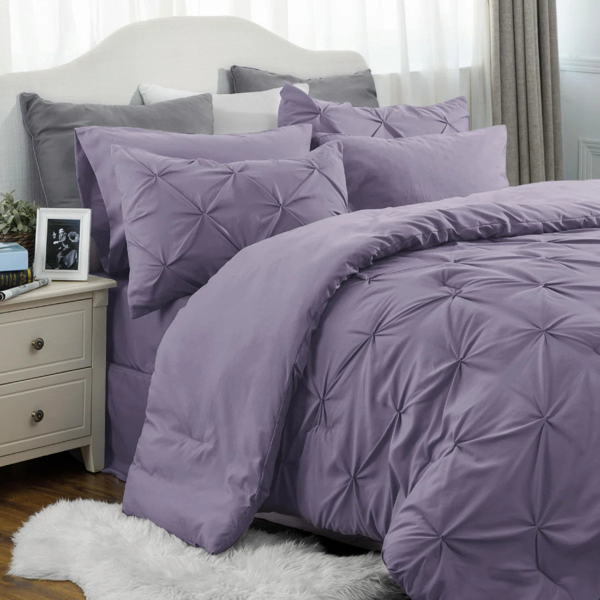 Purple bedding set on a bed with pillows and a nightstand in a bedroom.