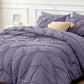 Purple textured comforter on a bed with pillows and a side table in the background.