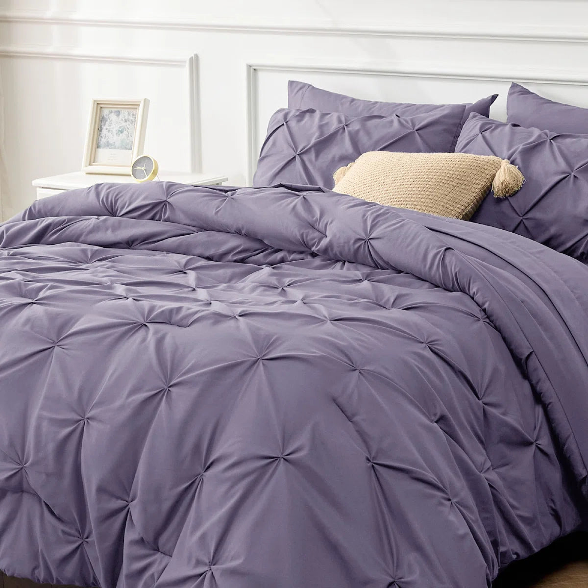Purple textured comforter on a bed with pillows and a side table in the background.