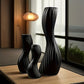 Three black decorative vases on a wooden surface with a blurred indoor background