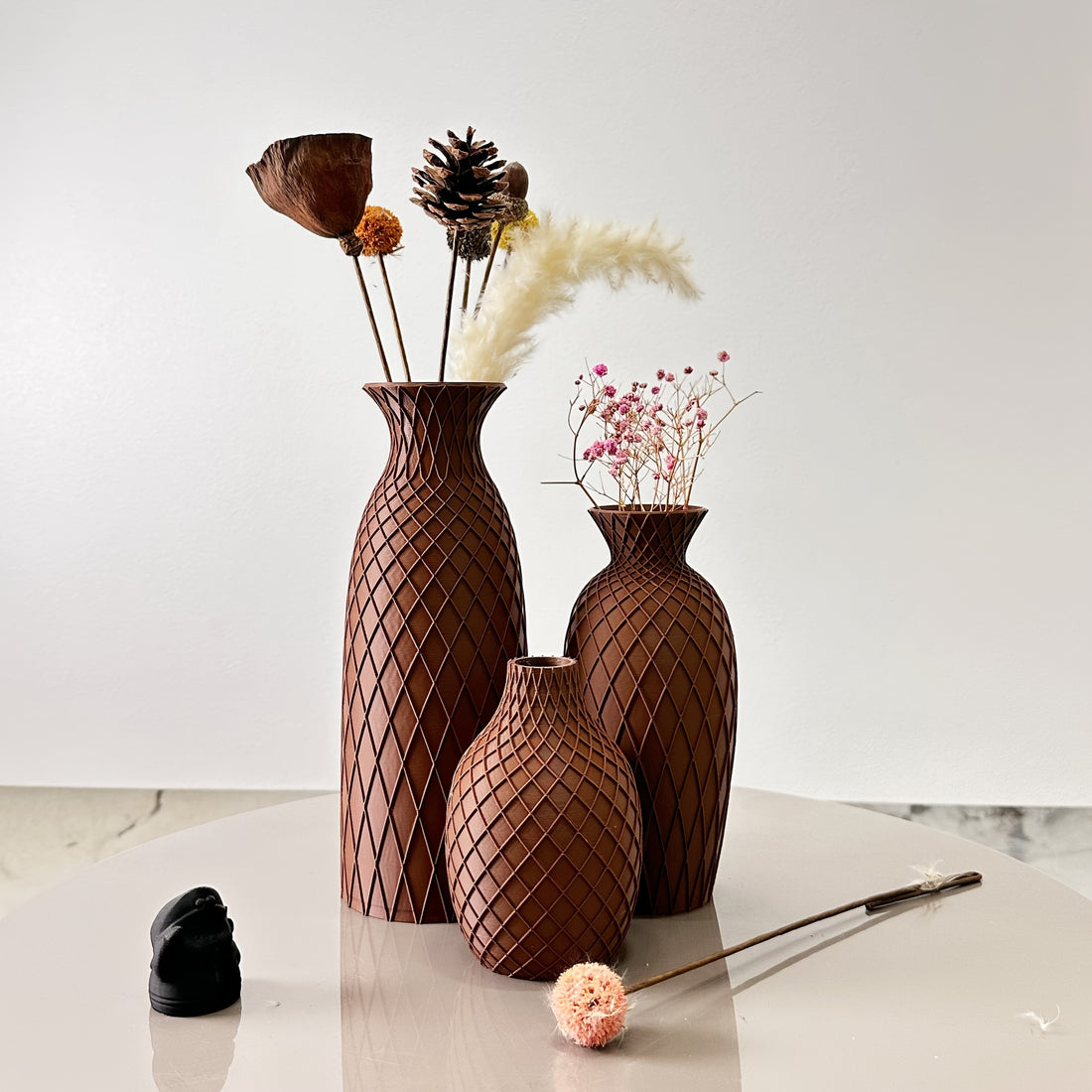 Set of three brown textured vases with decorative elements on a light surface.
