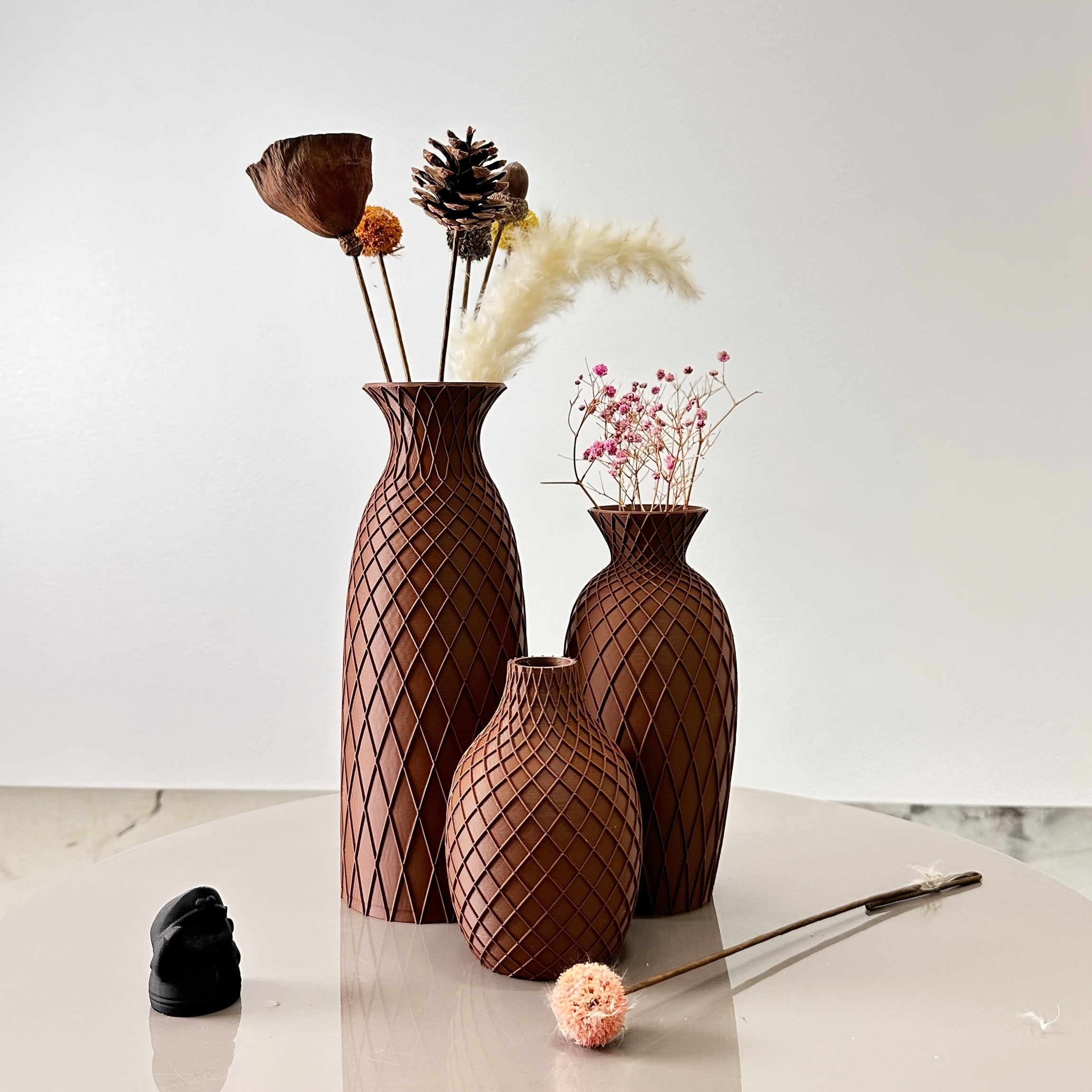 Set of three brown textured vases with decorative elements on a light surface.