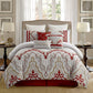Decorative bedspread with red and gold patterns on a bed in a well-lit bedroom.