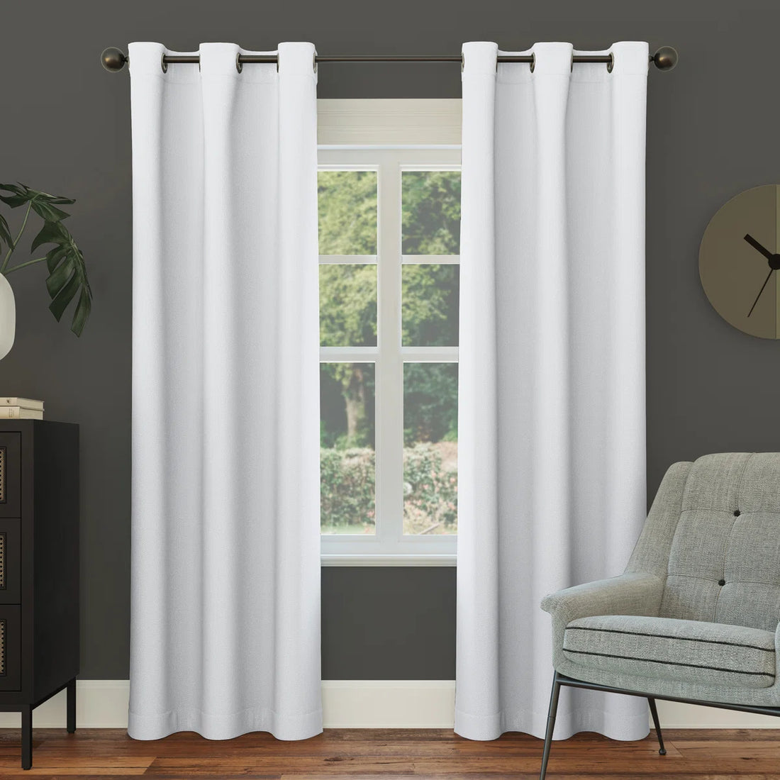 White curtains hanging in a room with a gray wall, window, and green chair.