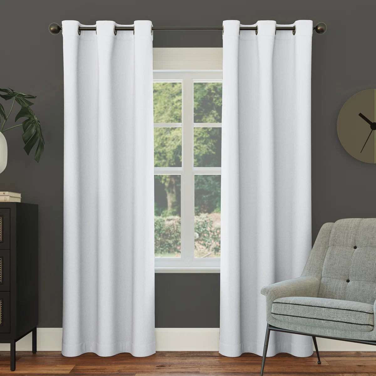 White curtains hanging in a room with a gray wall, window, and green chair.