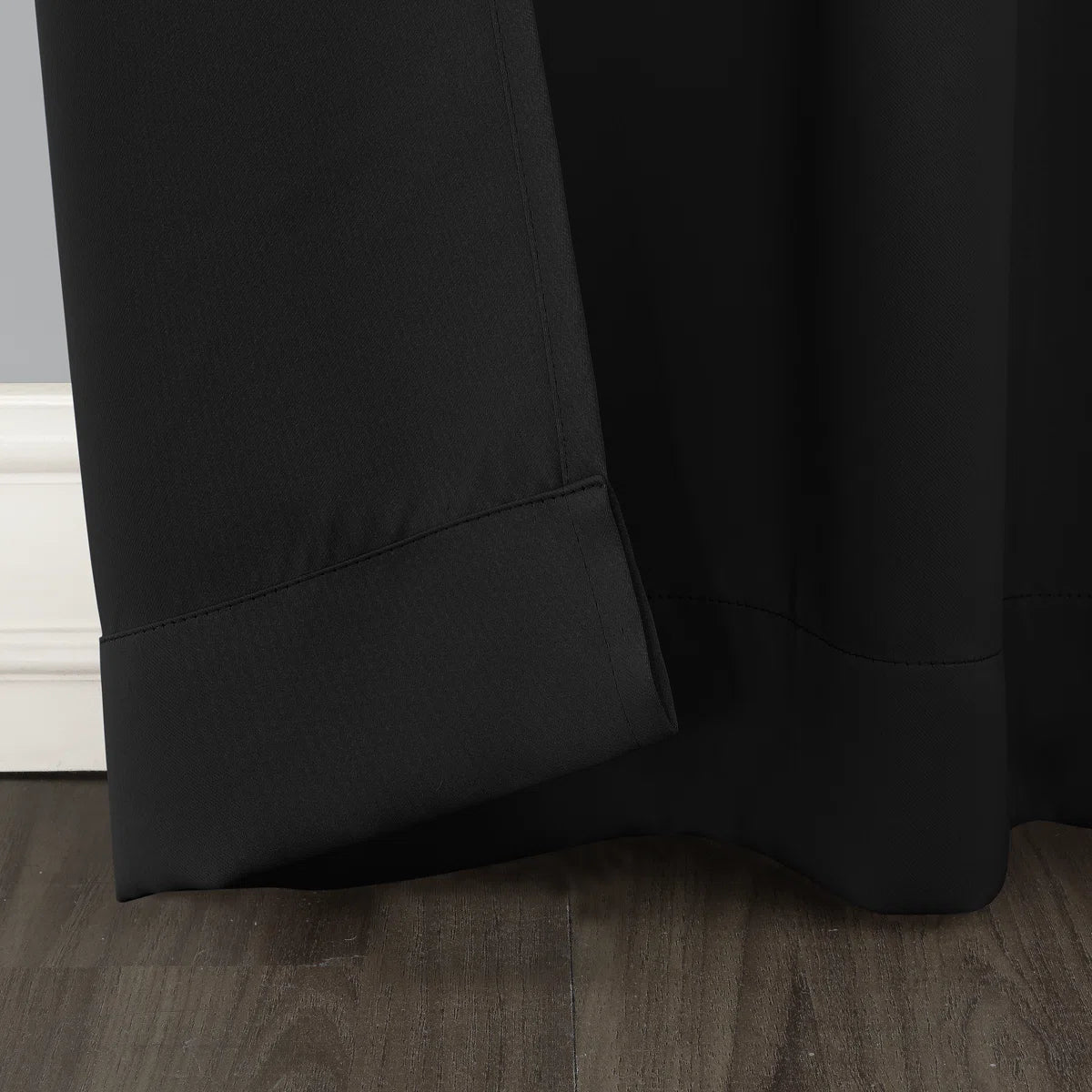Close-up of a black curtain on a wooden floor with a neutral wall background
